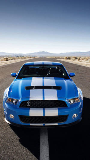 藍色 Shelby Mustang 帶白色條紋，在沙漠公路日落時分。 — F1 iPhone 壁紙