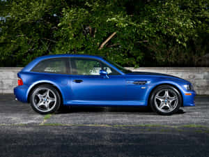 藍色BMW M3旅行車停在瀝青路上，靠近綠樹和石牆。 — Mercedes Benz C300 壁紙