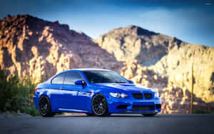 藍色BMW M3跑車停在沙漠公路上，背景是日落時分的山脈。 — Steam Deck OLED 壁紙
