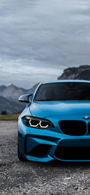 藍色BMW跑車停在碎石路上，靠近山脈，天空多雲。 — Pixel 8a 壁紙