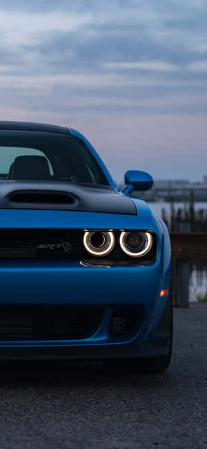 藍色Dodge Challenger SRT Hellcat，在黃昏時分帶有發光的頭燈。 — Pixel 8 壁紙