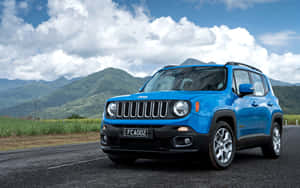 藍色Jeep Renegade SUV在山路上，有綠色山丘和多雲的天空。 — MacBook Pro M1 壁紙