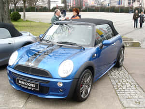 藍色MINI Cooper敞篷車停放在鵝卵石廣場上，附近有人。