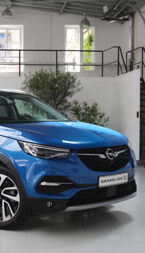 藍色Opel Grandland X SUV在現代工業展示間中，配有植物和窗戶。 — 華為Pura X View 壁紙