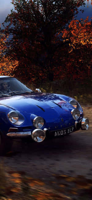一輛藍色經典拉力賽車在秋葉飄落的森林中疾馳。 — Pixel 11 Pro XL 壁紙
