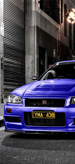 藍色日產Skyline R34停泊在黑暗小巷中，帶有塗鴉和霓虹燈光。 — Pixel 7 Pro 壁紙