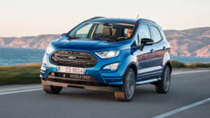 藍色福特 EcoSport 在日落時分沿海岸道路行駛，靠近海洋。 — 福特 壁紙