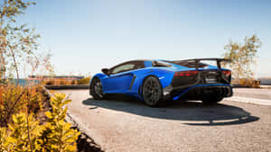 藍色藍寶堅尼 Aventador SVJ 停泊在沿海道路上，周圍有金色的樹葉和晴朗的天空。 — 汽車 壁紙