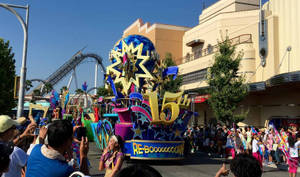 一輛節日遊行花車，帶有金色星星和「15th」字樣，穿過主題公園，人群圍觀。 — 環球影城 壁紙