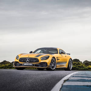 黃色 Mercedes-AMG GT R 在賽道上，配有藍色路緣石和綠色灌木叢。 — 跑車 壁紙