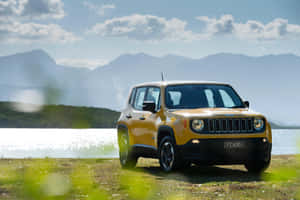 黃色Jeep Renegade停泊在湖邊，背景有山。 — Surface Pro 壁紙