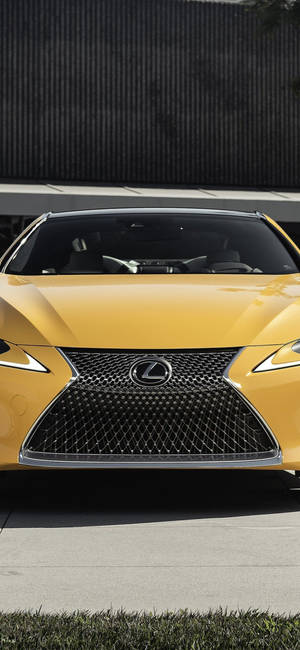 黃色Lexus跑車帶有獨特水箱護罩，停在深色牆壁附近。 — iPhone 16 Pro Max 壁紙
