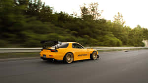 黃色跑車在高速公路上疾馳，背景有模糊的綠色樹木。 — 馬自達 壁紙