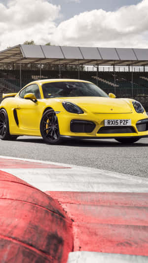 黃色保時捷 Cayman GT4 在設有紅白路緣的賽道上。 — 舊金山 iPhone 壁紙