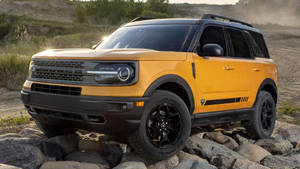 黃色福特Bronco SUV在沙漠景觀中行駛在岩石上。 — 老福特卡車 壁紙
