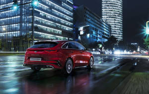紅色Kia Proceed旅行車在雨夜城市中行駛，燈光閃爍。 — 起亞 壁紙