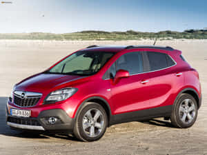 紅色Opel Mokka SUV停泊在沙灘上，靠近沙丘，天空清澈湛藍。 — 好看汽車 壁紙