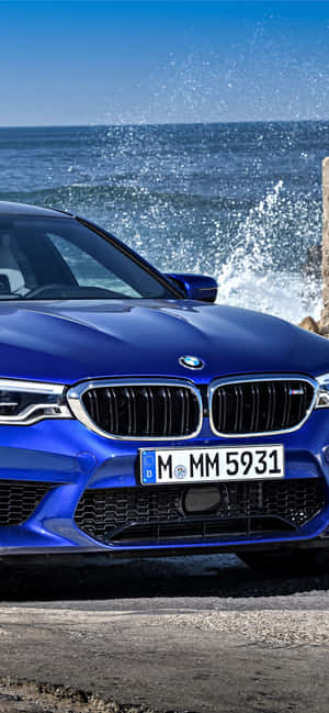 藍色BMW M5停泊在海洋旁邊，附近有浪花拍岸。 — iPhone Air 壁紙