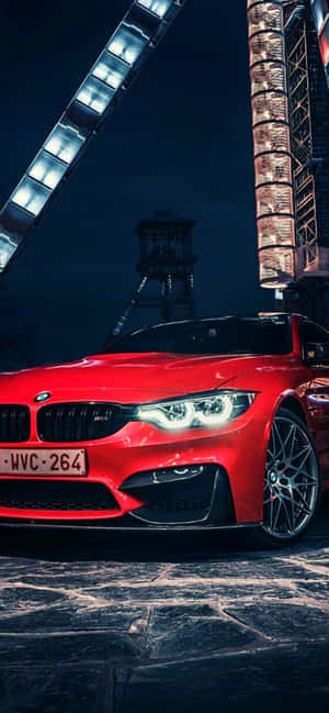夜晚在發光的霓虹招牌下，停在石頭街道上的紅色BMW M4。 — iPhone 13 Mini 壁紙