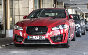 紅色Jaguar XF 550停放在城市環境中，光澤表面反射出周圍景象。 — Steam Deck 壁紙