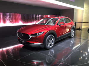 紅色Mazda CX-30 SUV在反射地板上，帶有閃爍粉紅色牆面顯示。 — 馬自達 壁紙