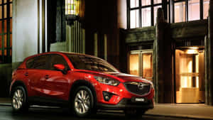 夜間停在一棟燈光明亮的建築前的紅色Mazda CX-5 SUV。 — 馬自達 壁紙