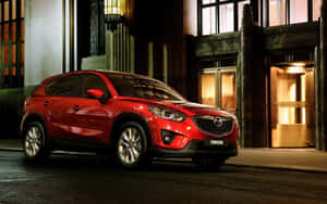 紅色Mazda CX-5 SUV夜間停泊在城市的街道上，靠近有燈光的建築入口。 — 馬自達 壁紙