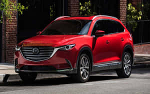 紅色Mazda CX-9 SUV停泊在城市街道上，靠近磚造建築。 — 馬自達 壁紙