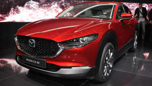 紅色Mazda CX-30 SUV在車展上展出，配有反光地板和抽象背景。 — 馬自達 壁紙