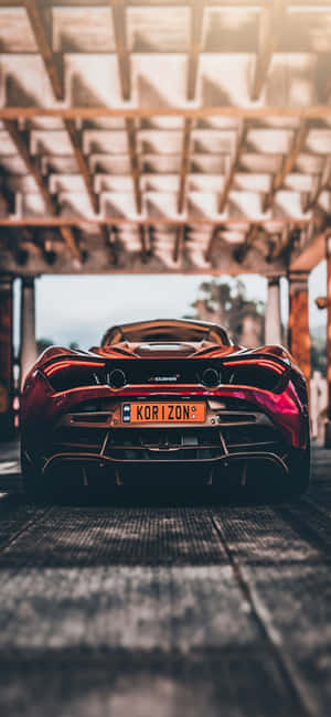 紅色McLaren跑車停放在木結構下，伴隨陽光光束。 — iPhone 14 Plus 壁紙