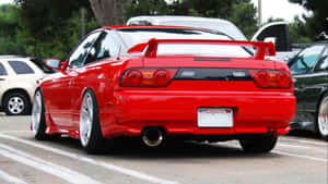 紅色日產Skyline R34跑車停放在停車場，背景有樹木和其他汽車。 — 日產 壁紙