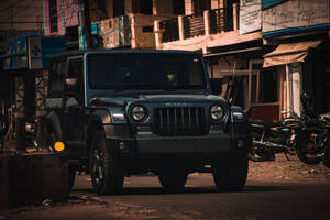 深綠色Mahindra Thar SUV停泊在塵土飛揚的街道上，伴隨著機車和建築物。