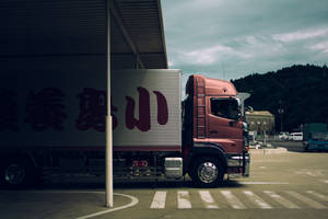 粉紅色送貨卡車停放在金屬遮陽篷下，後面有山丘。 — 卡車 壁紙