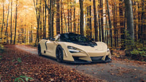 奶油色McLaren跑車在鋪滿秋葉的森林道路上。 — 汽車 壁紙