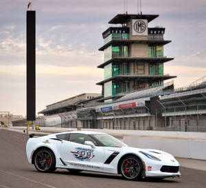 白色Corvette Indy 500 Pace Car在賽道上，背景有IMS塔和日落。 — 賽車 壁紙