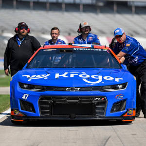 帶有Kroger標誌的藍色NASCAR賽車在賽道上被團隊工作人員推動。 — 跑車 壁紙