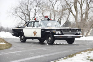 一輛經典的黑白警長車停在積雪的道路上，周圍是光禿禿的樹木。 — 克萊斯勒 壁紙