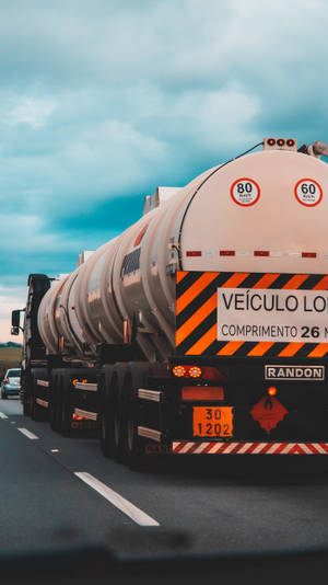 多雲天空下高速公路上帶有橙色危險條紋的銀色油罐車。 — 引擎油 壁紙