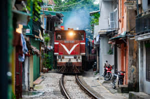 紅色火車在狹窄的城市小巷中行駛，旁邊有機車和色彩繽紛的建築物。 — 火車 壁紙