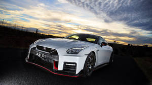 白色日產GT-R跑車帶紅色飾邊，停在日落時分的道路上。 — 日產 壁紙