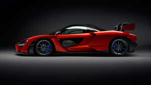 在攝影棚燈光下，帶有黑色飾件和藍色制動器的紅色McLaren Senna跑車。 — 麥拉倫 壁紙