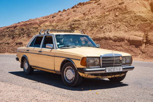 復古米色賓士計程車在沙漠公路上，有岩石山丘和藍天。 — Mercedes Benz C300 壁紙