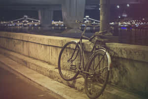夜晚河邊石欄杆旁靠著一輛腳踏車，背景有亮燈的橋樑。 — MacBook Air M3 壁紙