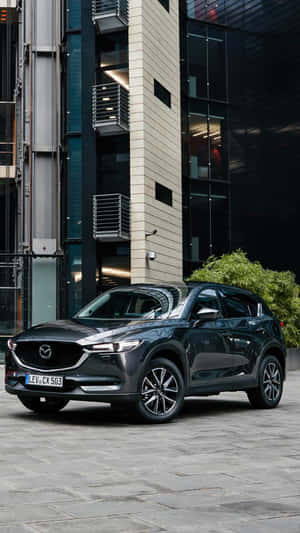 深灰色Mazda CX-5 SUV停放在一棟現代建築前面，建築有玻璃和混凝土外牆。 — 馬自達 壁紙