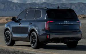 深藍色Kia Telluride SUV停泊在沙漠公路上，後面有山脈。 — Steam Deck 壁紙