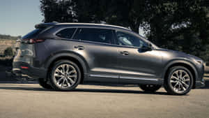 日落時分，灰色Mazda CX-90 SUV停泊在樹木附近的碎石路上。 — 馬自達 壁紙