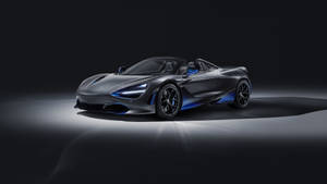 在黑暗的攝影棚環境中，一輛帶有藍色燈光點綴的啞光灰色McLaren 720S Spider。 — macOS Mojave 壁紙