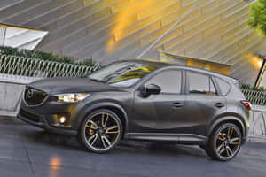 啞光灰色馬自達CX-5 SUV，金色輪圈，夜間停在現代建築附近。 — 馬自達 壁紙