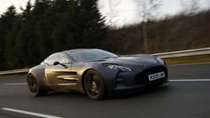 啞光黑色Aston Martin在日落時分的森林道路上奔馳。 — 奧斯頓馬丁 壁紙