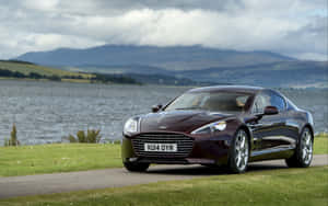 棗紅色Aston Martin停在湖邊，背景有山。 — Steam Deck 壁紙